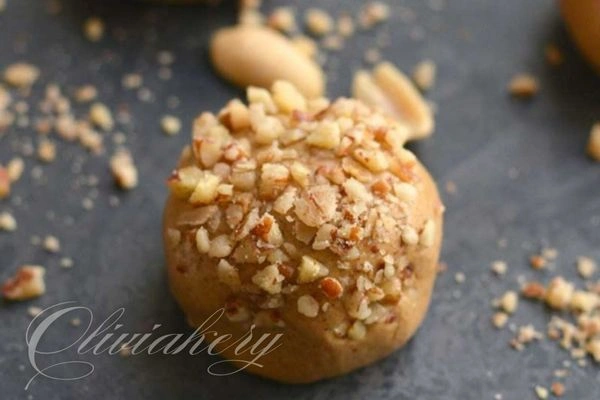 Peanut butter protein balls topped with chopped nuts on a dark surface.