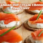 This is a close-up image of the Salmon Dill Cream Cheese Appetizer, served on a bed of creamy sauce atop crisp crackers and garnished with fresh chives.